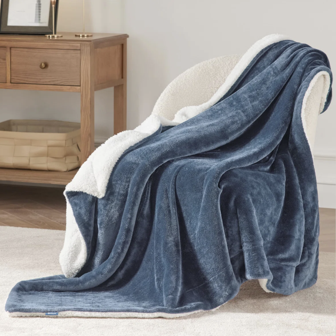 A plush blue blanket with a white sherpa lining draped over a chair, next to a wooden side table with decorative items.