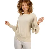 A woman is wearing a light beige long-sleeve top with flowing sleeves and a fitted waist, paired with light-colored pants.