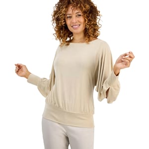 A woman is wearing a light beige long-sleeve top with flowing sleeves and a fitted waist, paired with light-colored pants.