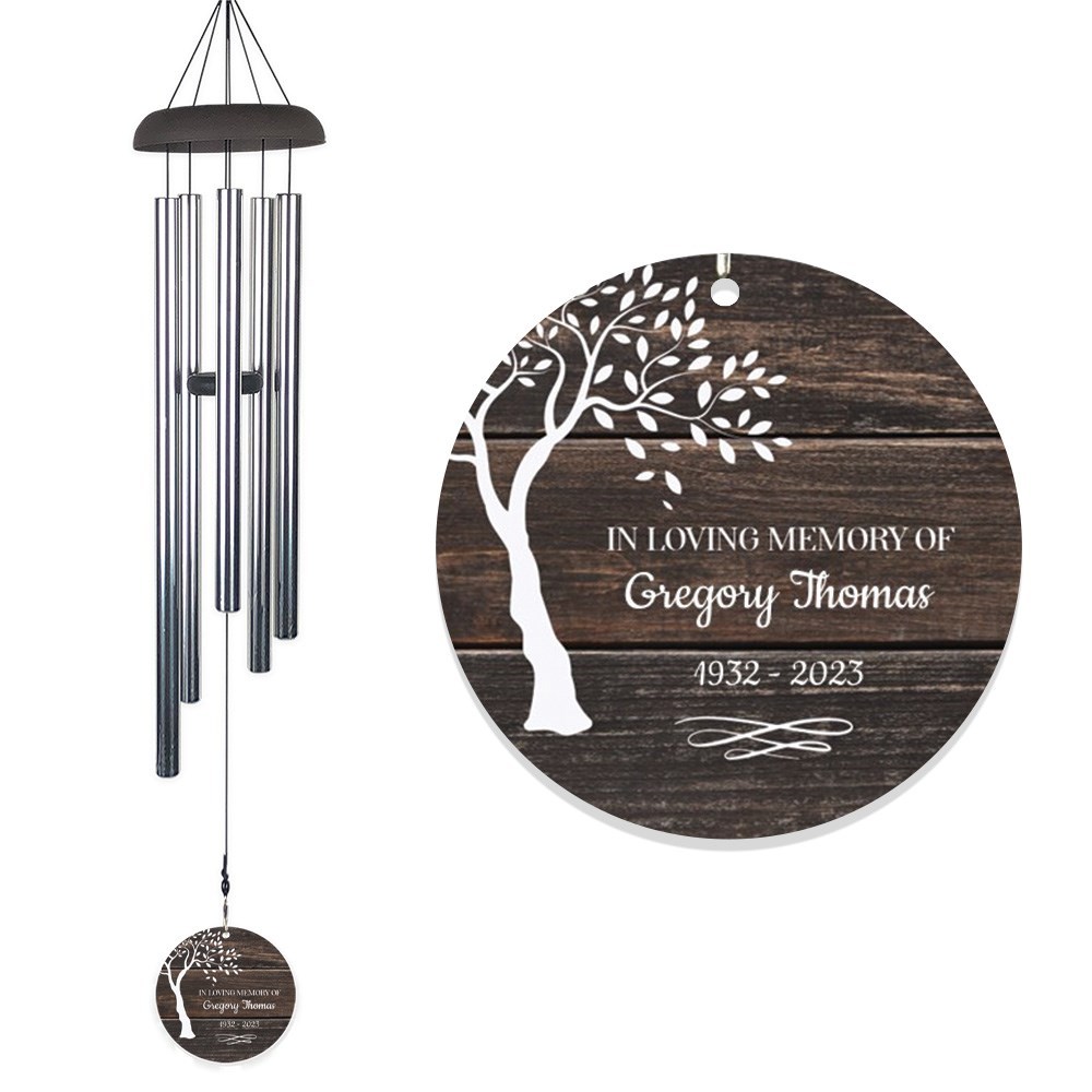 Personalized memorial wind chimes feature a wooden round disk with \“In Loving Memory of Gregory Thomas\“ and tree design, dated 1932-2023, hanging from silver tubes.