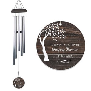 Personalized memorial wind chimes feature a wooden round disk with \“In Loving Memory of Gregory Thomas\“ and tree design, dated 1932-2023, hanging from silver tubes.