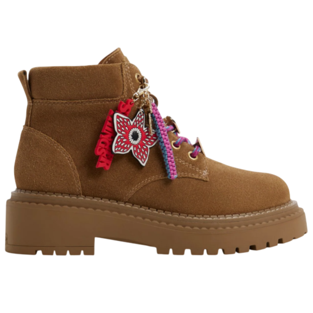 Brown suede ankle boot with chunky sole, pink and purple laces, and decorative charms featuring a flower and stylized text.
