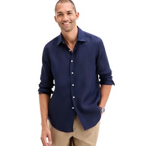 Man wearing a navy button-up shirt with rolled-up sleeves and beige pants, standing in a relaxed pose.