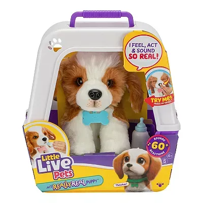 A toy puppy with a white and brown fur pattern sits inside a plastic carrying case, accompanied by a bottle accessory; packaging highlights over 60 sounds and actions.