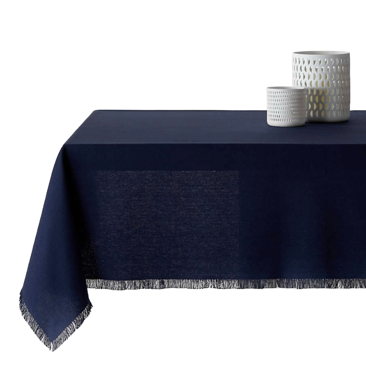 A dark blue tablecloth with fringe detailing is draped over a table, accompanied by two white, textured cylindrical vases on top.