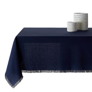 A dark blue tablecloth with fringe detailing is draped over a table, accompanied by two white, textured cylindrical vases on top.