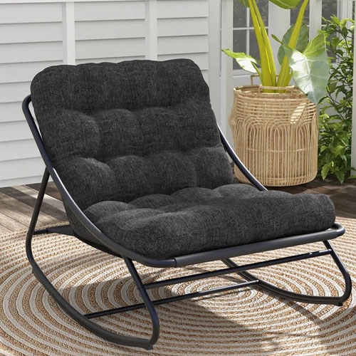 A cushioned black rocking chair with a metal frame is placed on a circular woven rug, accompanied by a wicker planter with a green plant next to it.
