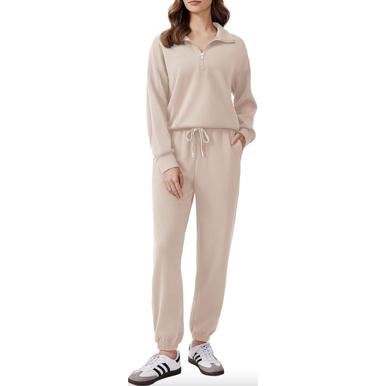 A woman is wearing a beige tracksuit with a half-zip sweatshirt top and matching drawstring joggers, paired with white and black sneakers.