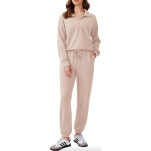 A woman is wearing a beige tracksuit with a half-zip sweatshirt top and matching drawstring joggers, paired with white and black sneakers.