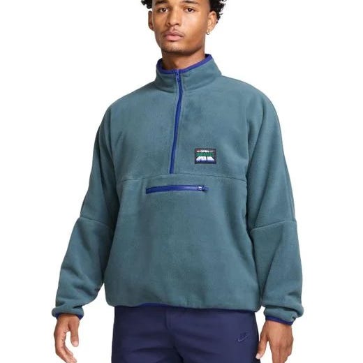 Nike Club Men's Half-Zip Fleece Pullover in teal with a high collar, chest logo patch, and front zippered pocket. Designed for warmth and casual style, featuring a relaxed fit and navy accents.