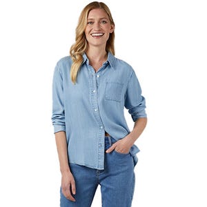 A person wearing a light blue denim shirt with buttons and a chest pocket, paired with darker blue jeans.