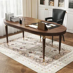 An oval wooden desk with brass accents sits on a patterned rug, accompanied by a black chair. The desk holds books, pens, and stationery items in an elegant office setting.