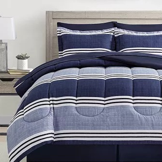 A bedding set with a striped pattern in navy and white is displayed on a bed with matching shams. The room includes a wooden headboard, side tables with lamps, and framed abstract artwork on the wall.