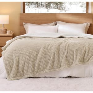 A cozy queen-size Sherpa blanket with a soft, textured pattern in a light beige color is neatly spread over a bed with white pillows, a wooden headboard, and a nightstand on the side, in a well-lit room with snow visible through the window.