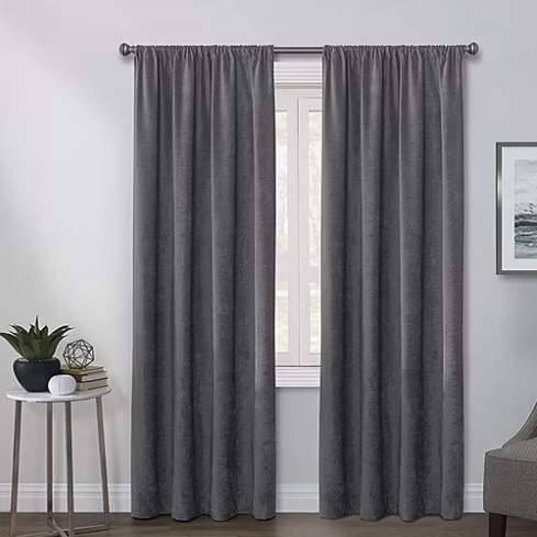 A pair of gray curtains hangs on a metal rod against a window, accompanied by a side table with decorative items.