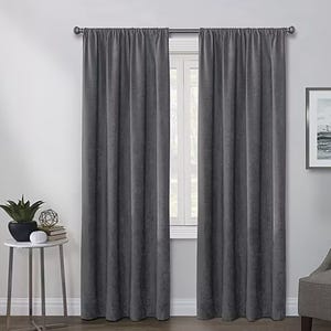 A pair of gray curtains hangs on a metal rod against a window, accompanied by a side table with decorative items.
