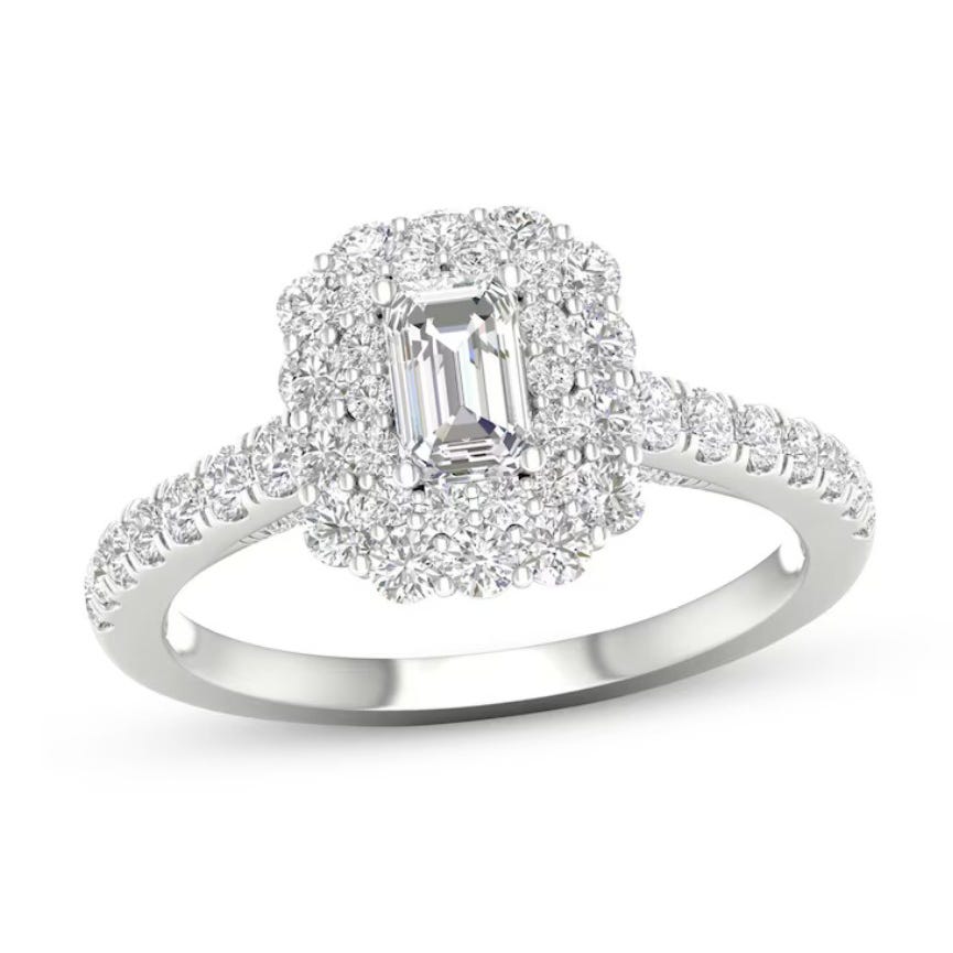 A white gold ring featuring an emerald-cut center diamond surrounded by a halo of smaller diamonds, with additional diamonds set along the band.