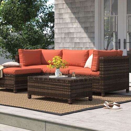 a brown woven patio set with orange cushions on a patio in the daytime