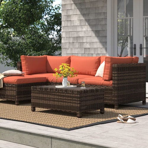 a brown woven patio set with orange cushions on a patio in the daytime