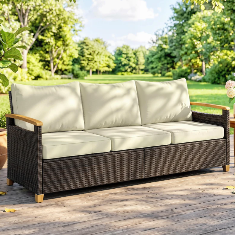 Outdoor wicker sofa with cream cushions and wooden armrests, set on a wooden deck in a garden setting.