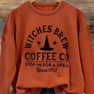 Orange sweatshirt with \“Witches Brew Coffee Co. Stop in for a Spell Since 1962\“ printed on it, featuring a witch's hat and star design.