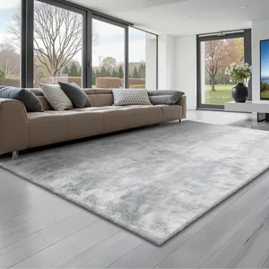 Contemporary living room with a large, gray area rug on light wood flooring, a tan sofa with assorted pillows, and floor-to-ceiling windows offering a view of a landscaped garden.