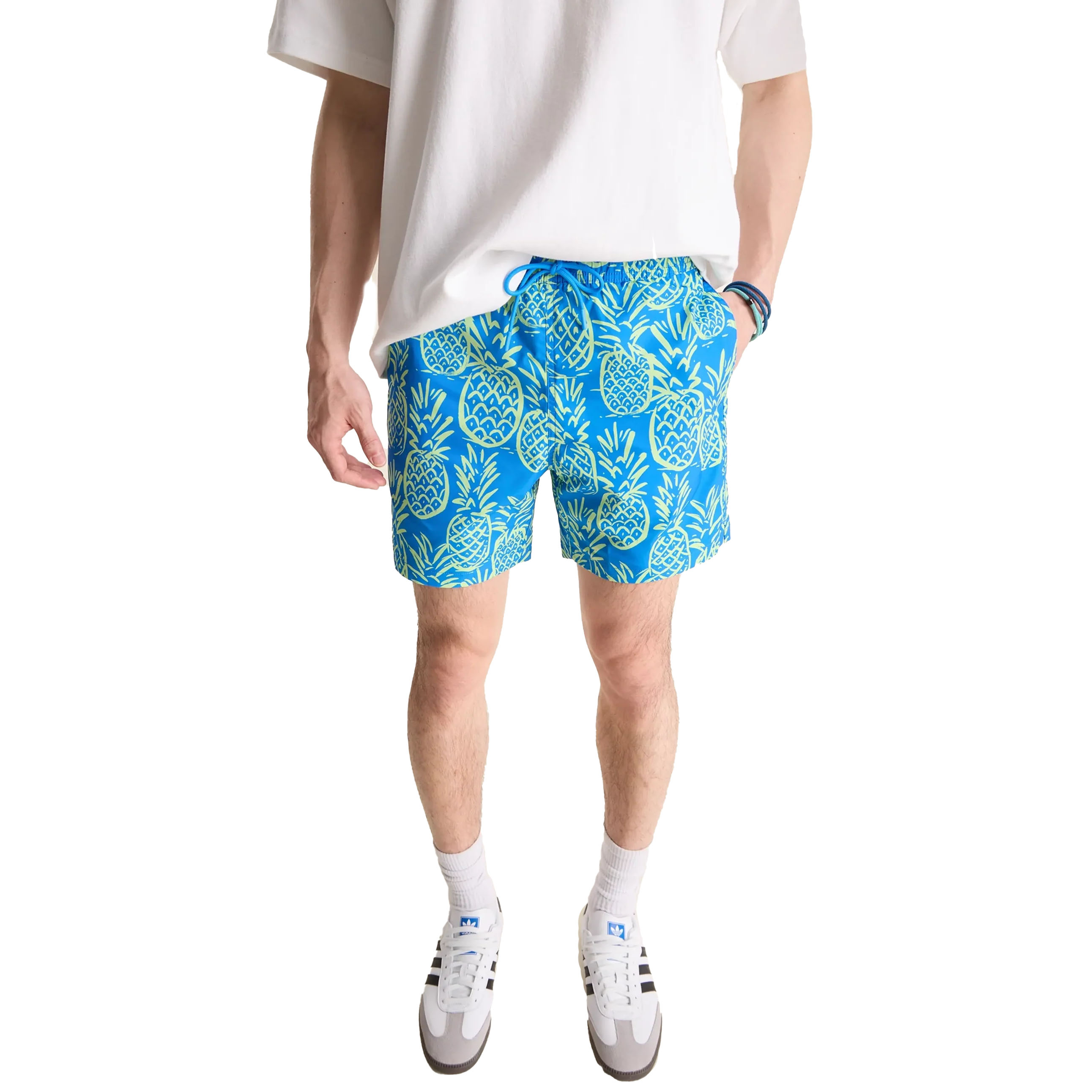Blue shorts featuring a vibrant pineapple pattern, paired with a casual white T-shirt and sporty white sneakers with black stripes.