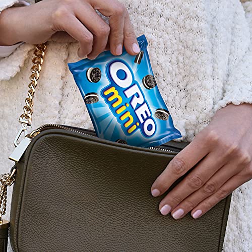 A person is holding a small blue pack of Oreo Minis over a green handbag.