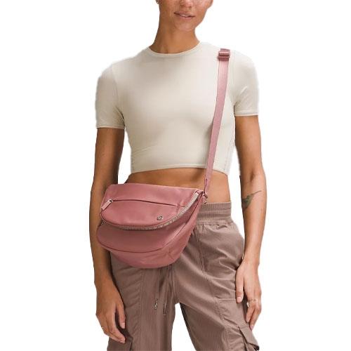 Woman in a cropped beige top and brown cargo pants, wearing a pink crossbody bag with a zippered compartment.