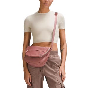 Woman in a cropped beige top and brown cargo pants, wearing a pink crossbody bag with a zippered compartment.