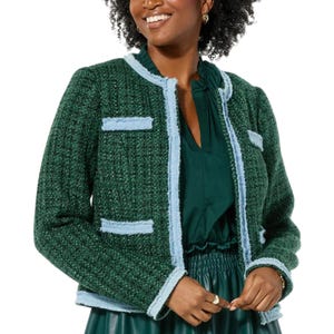 A woman is wearing a green tweed jacket with light blue trim over a green dress.