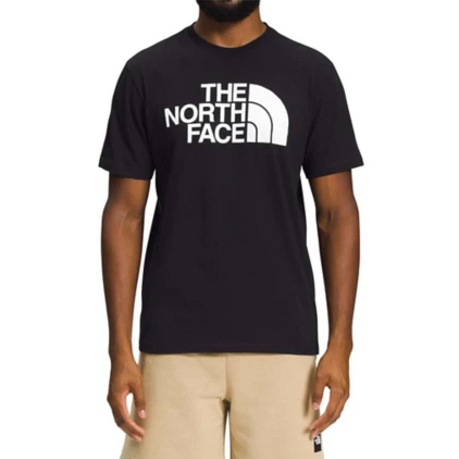A person wearing a black T-shirt with a white \“The North Face\“ logo on the chest, paired with beige shorts.