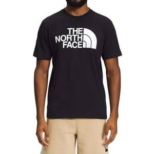 A person wearing a black T-shirt with a white \“The North Face\“ logo on the chest, paired with beige shorts.