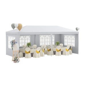 White party tent with windows, featuring round tables and chairs adorned with cream-colored covers and yellow bows, floral decorations, and balloons.