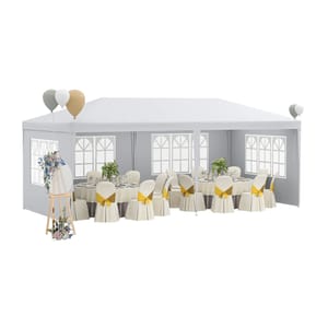 White party tent with windows, featuring round tables and chairs adorned with cream-colored covers and yellow bows, floral decorations, and balloons.