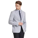 A man is wearing a light gray blazer, a white dress shirt, a dark tie, black dress pants, and black leather shoes.