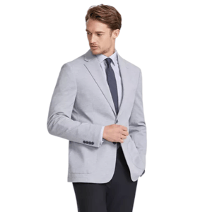 A man is wearing a light gray blazer, a white dress shirt, a dark tie, black dress pants, and black leather shoes.