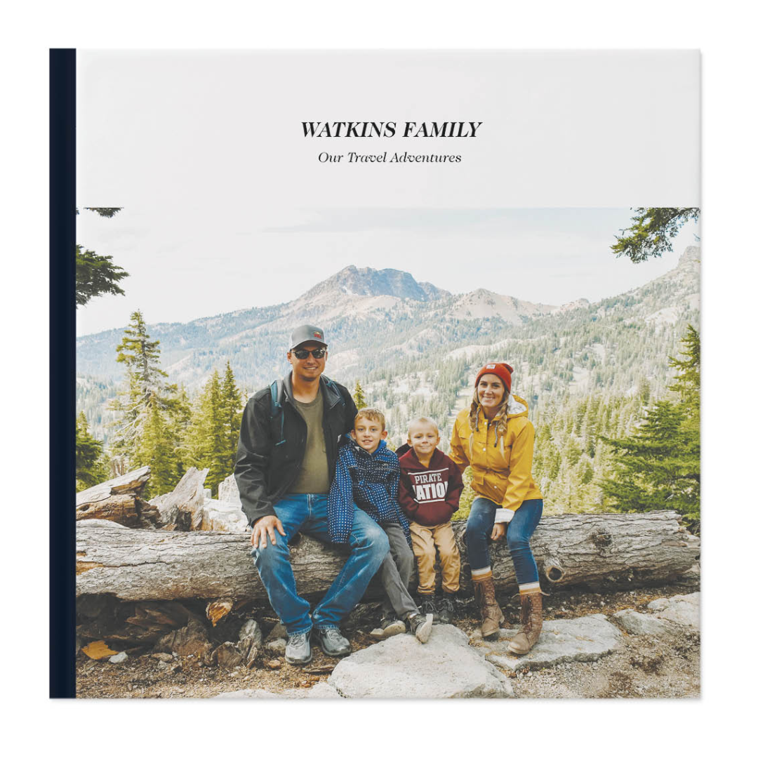 Photobook cover titled \“Watkins Family: Our Travel Adventures\“ featuring a family of four sitting on a log with a mountainous forest background.