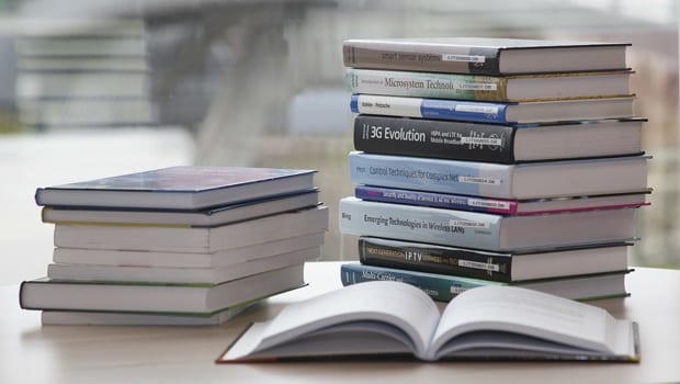 Two stacks of academic books on a table, with one opened book in the foreground.