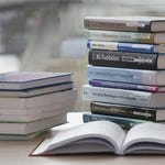 Two stacks of academic books on a table, with one opened book in the foreground.