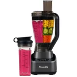 A PowerXL blender and a matching travel cup with pink smoothie inside, both on a white brick backdrop. The blender contains chopped mango, cucumber, and carrot.