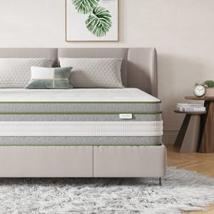 Novilla Queen-Size Vitality Mattress features a multi-layered design with gray and white fabric and green accents, set in a modern bedroom with a cushioned headboard, decorative pillows, and a bedside table featuring a clock and plant.