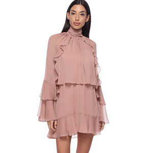 A woman is wearing a light pink tiered dress with ruffled sleeves and a high collar. The dress has a flowing, layered design.