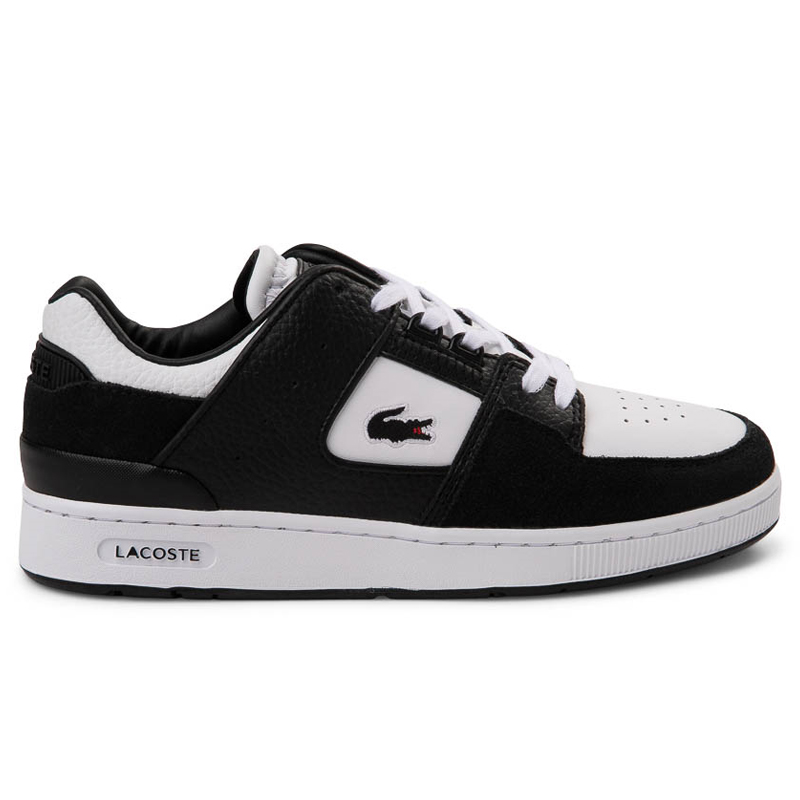 The Lacoste Women's Court Cage Athletic Shoe features a black and white color scheme with a leather upper, signature crocodile logo on the side, and a cushioned white sole for comfort and style.