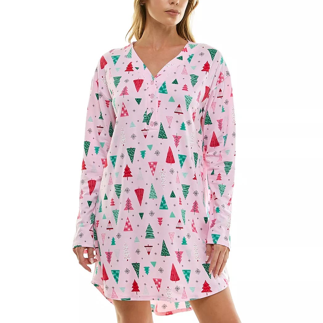 A woman is wearing a pink long-sleeve nightshirt with a festive pattern of red and green Christmas trees and snowflakes.