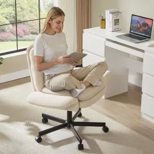 A person sits cross-legged on a beige, cushioned swivel office chair using a tablet. Nearby is a white desk with a laptop, books, and a pencil holder, set in a bright room with a large window.