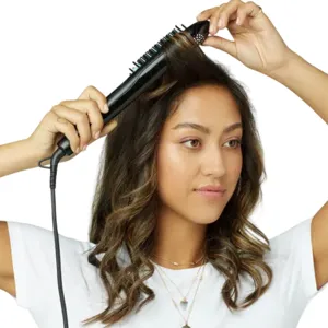 A person uses a heated straightening brush to style their wavy hair.