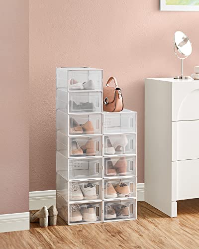 A stack of 12 clear plastic shoe storage boxes, each with a front opening for easy access, arranged against a wall beside a furniture piece.