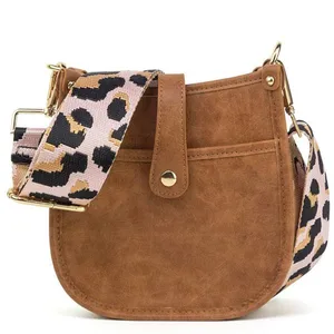 Brown faux leather crossbody bag with gold hardware, featuring a buttoned flap and a wide, detachable strap with a leopard print design.