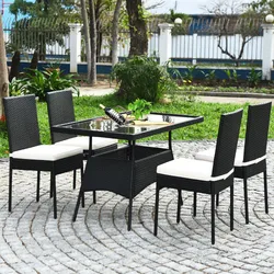 Outdoor patio set featuring a rectangular glass-top table and four black wicker chairs with white cushions, placed on a cobblestone surface in a garden setting.